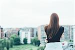 Rear view of young woman with long red hair looking out over cityscape