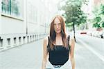 Portrait of freckled young woman with long red hair standing on city street