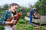 Young couple in chicken coop holding chicken