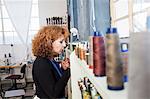 Woman in sewing workshop selecting thread from shelf