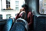 Young woman sitting on bus, wearing headphones, looking out of window