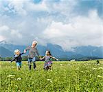 Grandmother and grandchildren running in field holding hands, Fuessen, Bavaria, Germany