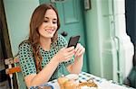 Woman at pavement cafée looking at smartphone smiling