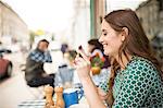 Side view of woman at pavement cafée looking at smartphone smiling