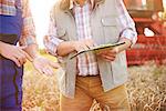 Cropped view of farmers in wheat field looking at clipboard