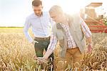 Farmer and businessman in wheat field quality checking wheat