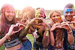 Portrait of group of friends at festival, covered in colourful powder paint, making heart shapes with hands