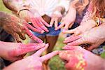 Group of friends at festival, covered in colourful powder paint, connecting fingers with peace signs, close-up