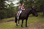 Girl and woman sitting bareback on horse in forest glade, Sattelbergalm, Tyrol, Austria