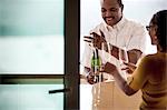 Middle aged African American couple celebrating success and opening bottle of champagne on house deck.