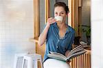 Young woman sitting at bar in cafée, drinking coffee, holding book