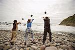 Mature man with his teenage grandchildren throwing rocks into the sea.