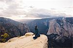 Young woman wrapped in blanket, standing at top of mountain, overlooking Yosemite National Park, California, USA