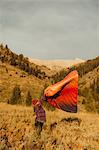 Pregnant woman standing in field, shaking out sleeping bag, Mineral King, Sequoia National Park, California, USA