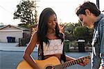 Young couple outdoors, young woman playing guitar