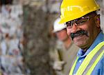 Portrait of mature male worker in hard hat, in front of stacked rubbish at recycling plant