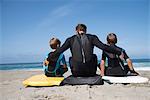 Rear view of man and two sons sitting on bodyboards, Laguna Beach, California, USA