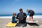 Rear view of father and two sons practicing with bodyboards on beach, Laguna Beach, California, USA