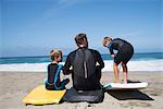 Rear view of father and two sons practicing with bodyboards on beach, Laguna Beach, California, USA