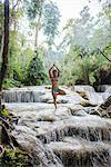 Woman standing on one leg, in tree pose, in Kuang Si waterfall, Luang Prabang, Laos