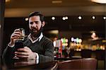 Man having glass of drink while using mobile phone