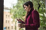 Businesswoman holding disposable coffee cup and using mobile phone