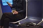 Businesswoman with coffee cup and luggage using phone while sitting in train