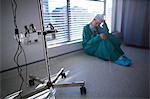 Tensed female surgeon sitting in corridor