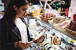 Woman looking at meat display while using mobile phone