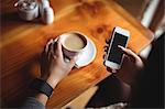 Woman using mobile phone while having a cup of coffee