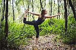 Woman performing standing bow pose yoga in forest