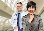 Happy Mixed Race Woman Looking To The Side As Male Doctor Stands Behind Her Inside Hospital.