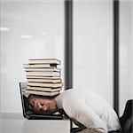 Businessman on laptop with a pile of books on head. Oppressed by work concept