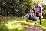 Father Pushing Children On Tire Swing In Garden