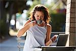 Woman using smartphone and laptop drinking coffee outside