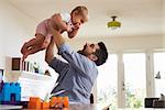 Father Sits At Table And Plays With Baby Son At Home