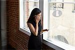 Businesswoman Making Phone Call Standing By Office Window