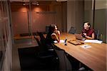 Two businesswomen working late in an office share a joke