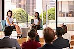 Two female speakers sit facing audience at business seminar