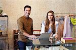 Young man and woman working in clothes shop look to camera