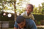 Young black boy playing on his dadÕs back in a garden