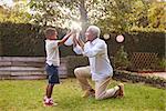 Black grandfather plays with grandson in garden, full length