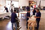 Carpenters Working On Machines In Busy Woodworking Workshop