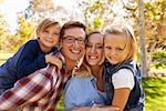 Parents carrying their two young kids in park look to camera