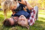 Two young kids lying on top of their dad in a park