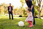 Parents kicking a ball with their young daughter in a park