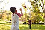Dad and son throwing American football to each other in park