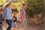 Young white family walking on a path in sunlight, side view