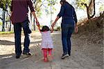 Parents and young daughter walk hand in hand on a rural path