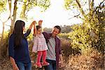 Mixed race couple walk on rural path lifting young daughter